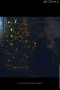 Óleo de una persona sentada en la oscuridad con un árbol de Navidad decorado e iluminado al lado.